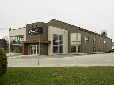 Grey building with a sign that reads 'Palais Centre-Ville' beside an empty parking lot and grass.