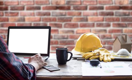 Engineer working on a laptop at a desk, his coffee mug and yellow hardhat on the table beside him