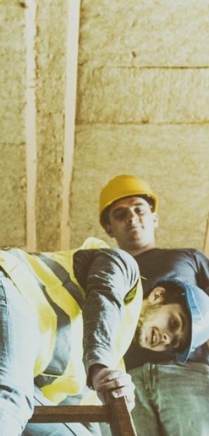 Un ouvrier en construction observe pendant qu’un autre descend une échelle d’un grenier fraîchement isolé.